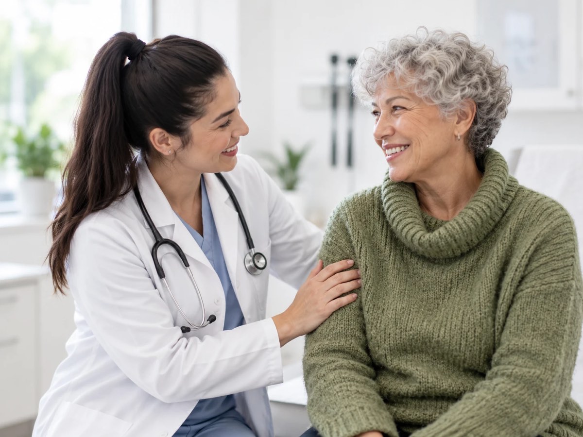 A physician rests a reassuring hand on an older patient's shoulder during a visit at a medical practice.
