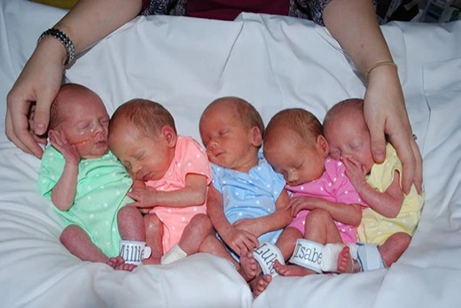 Five newborns cradled in their parents' hands